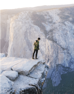 A man stands on the edge of a cliff, looking down.